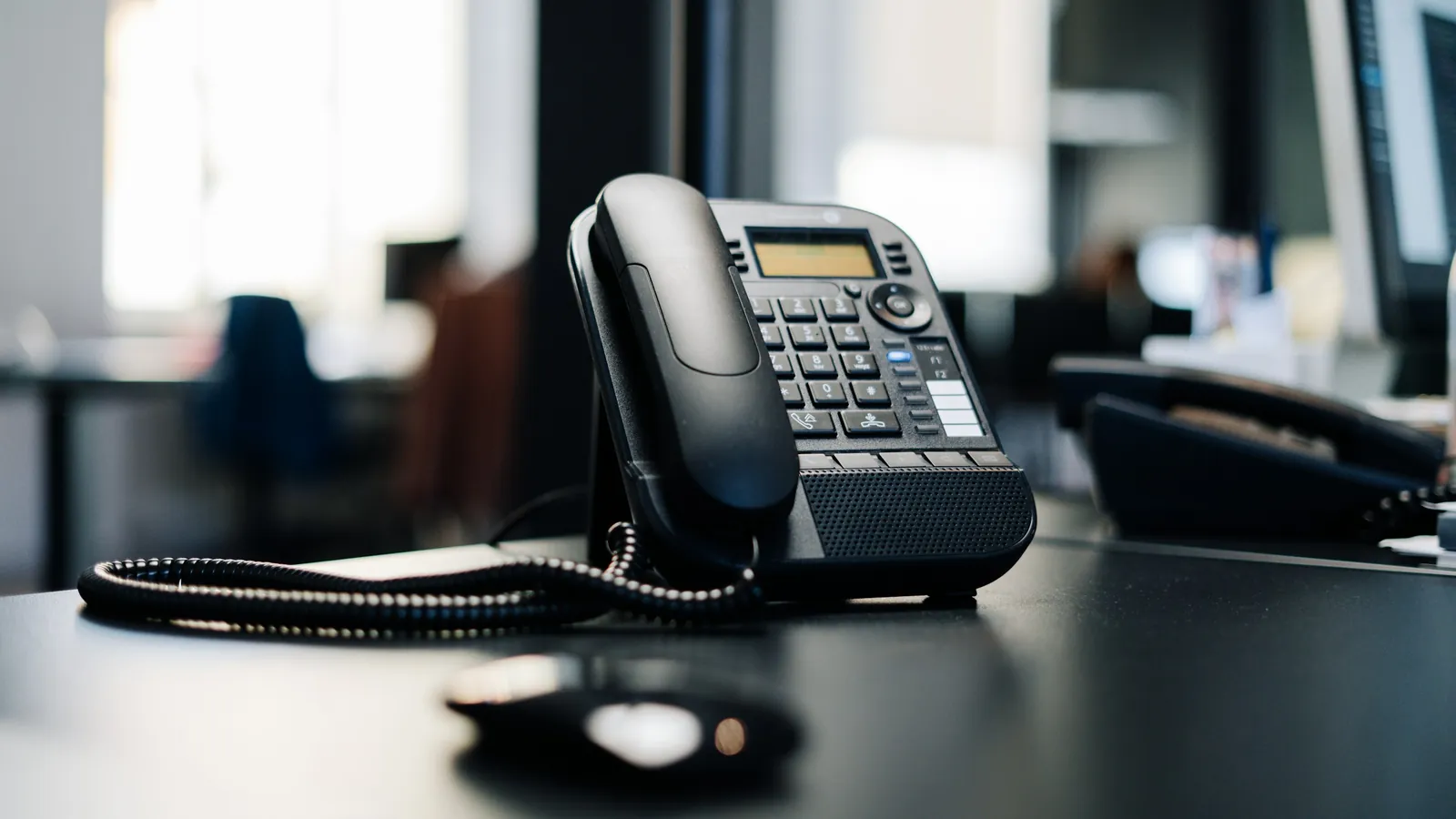 Black desk phone on an office desk with the handset in its cradle